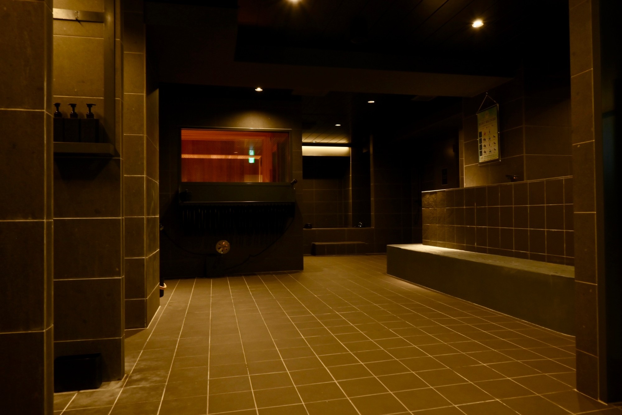 sauna KOHAKUの浴室。落ち着いた照明のタイル張りの空間にサウナ室の入口が見える